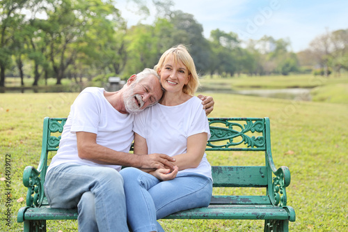 elderly caucasian couple with white shirt and blue jean sitting and embracing in park during summer time on wedding anniversary day © feeling lucky