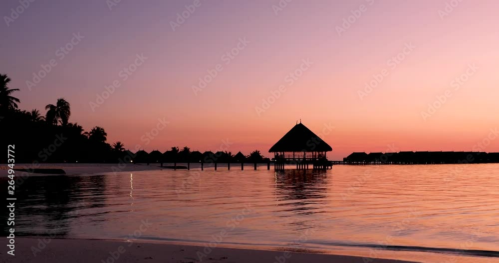 Sunset over a tropical beach in the Maldives with coconut pakm trees and over water lodges Sunset over a tropical beach in the Maldives with coconut pakm trees and over water lodges