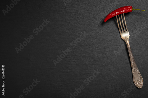 Papryczka chili nadziana na starym ozdobnym widelcu na czarnym tle kamienia łupkowego