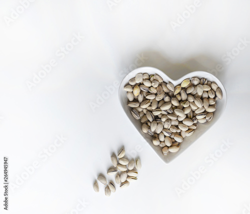 Nuts arranged in heart  on background. Healthy Food image close up pistachios on the cup plate. Love Texture on white grey table top view mock up