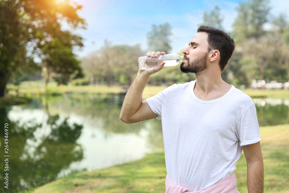 young man wearing sportswear standing and drinking pure water while exercising in the park young man wearing sportswear standing and drinking pure water while exercising in the park
