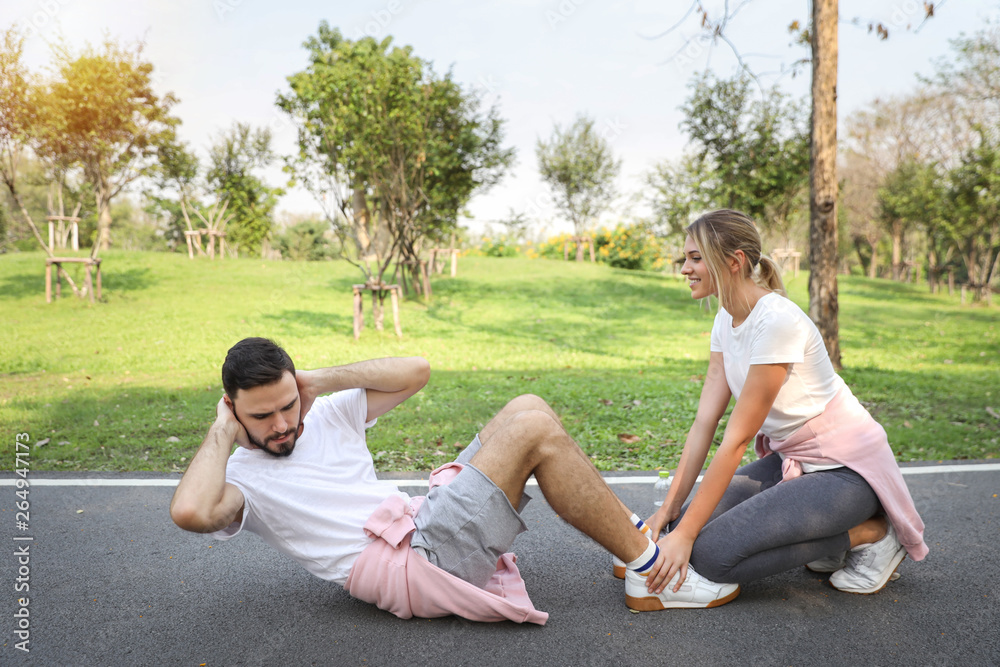 a runner couple is jogging in the park and doing sit up with a girlfriend holding his legs (healthy or sport concept) a runner couple is jogging in the park and doing sit up with a girlfriend holding his legs (healthy or sport concept)