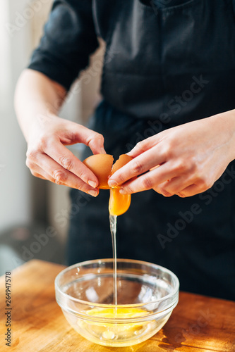 Female chef cracking eggs into a glass bowl