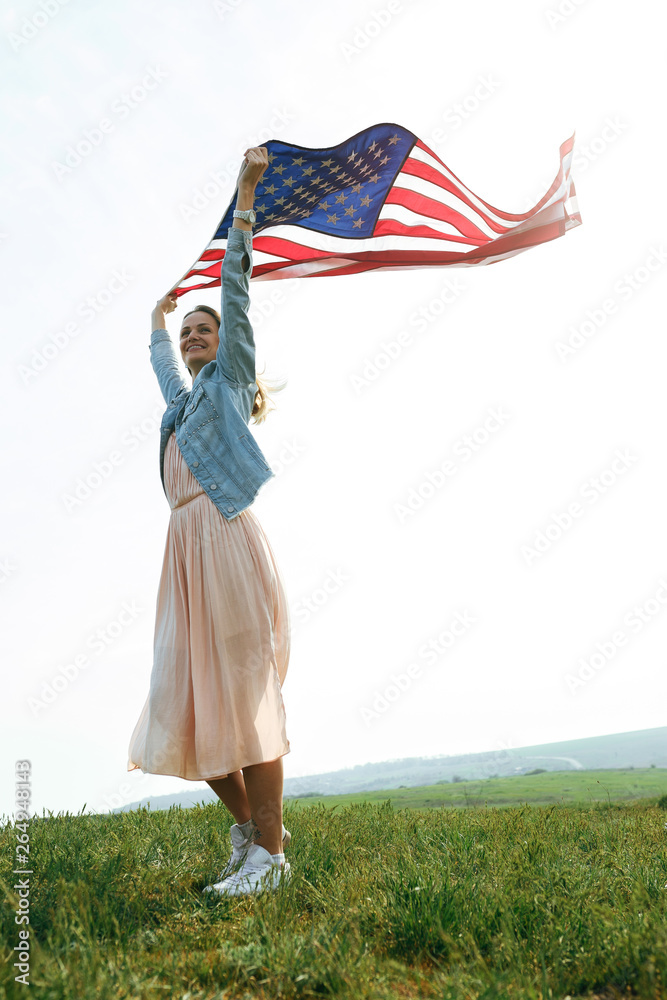 A girl in a coral dress and a denim jacket holds the flag of the united states in her hands. July 4th Independence Day.