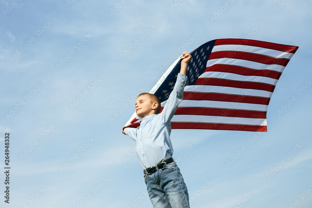 A little boy holds a flag of the United States against the sky. July 4th Independence Day.