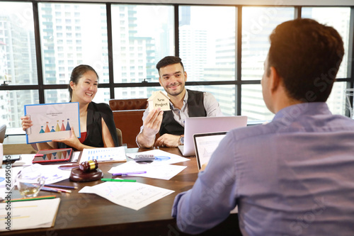 two caucasian businessmen having meeting with asian businesswoman. They use computer with chart, coffee cup and calculator beside while holding house model for new project with smiling face