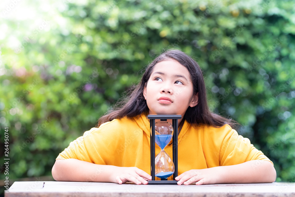 Little Asian girl is looking at the hourglass with feelings of loneliness Little Asian girl is looking at the hourglass with feelings of loneliness