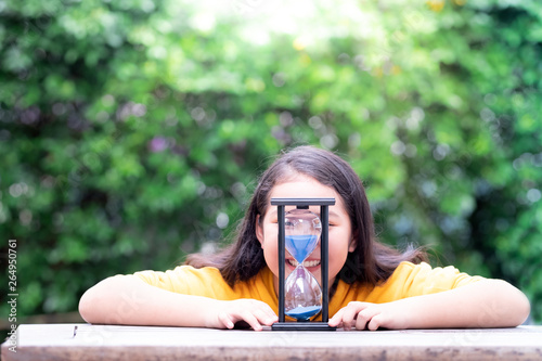 Little Asian girl is smiling behind the hourglass with feelings of happiness photo