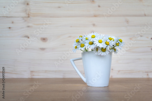 Bunch of fresh blooming daisies in a white porcelain cup on wooden table with wooden background. Hello spring or spring flowers background