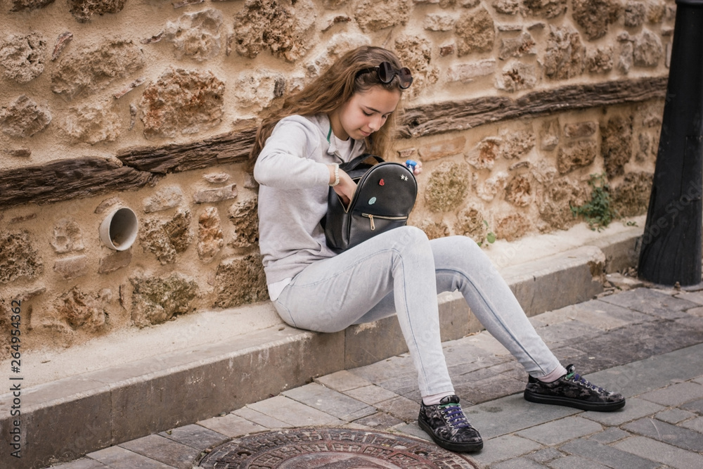 Young teen girl rummaging in a backpack sitting on the steps of the old house Young teen girl rummaging in a backpack sitting on the steps of the old house