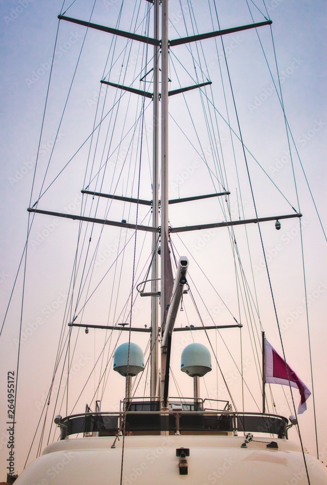 Obraz premium Mast of a luxury sailing yacht with sails down showing the rigging against a multi-colored sky