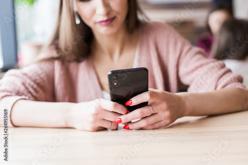 Attractive young woman sits at a table in a cafe with a cup of coffee and enjoys a laptop and smartphone