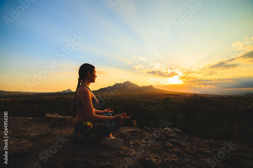 Young woman practicing yoga or pilates at sunset or sunrise in beautiful mountain location.