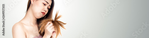 Fotografia Beauty hairstyle concept from Asian young woman unhappy, frustrated touch her hair in hand with looking at her dry and damaged long hair, for website where you place banner ads