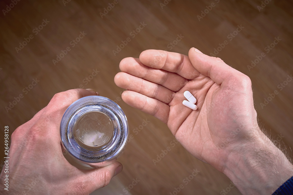 Fototapeta premium Male holding pills in hand and glass of water