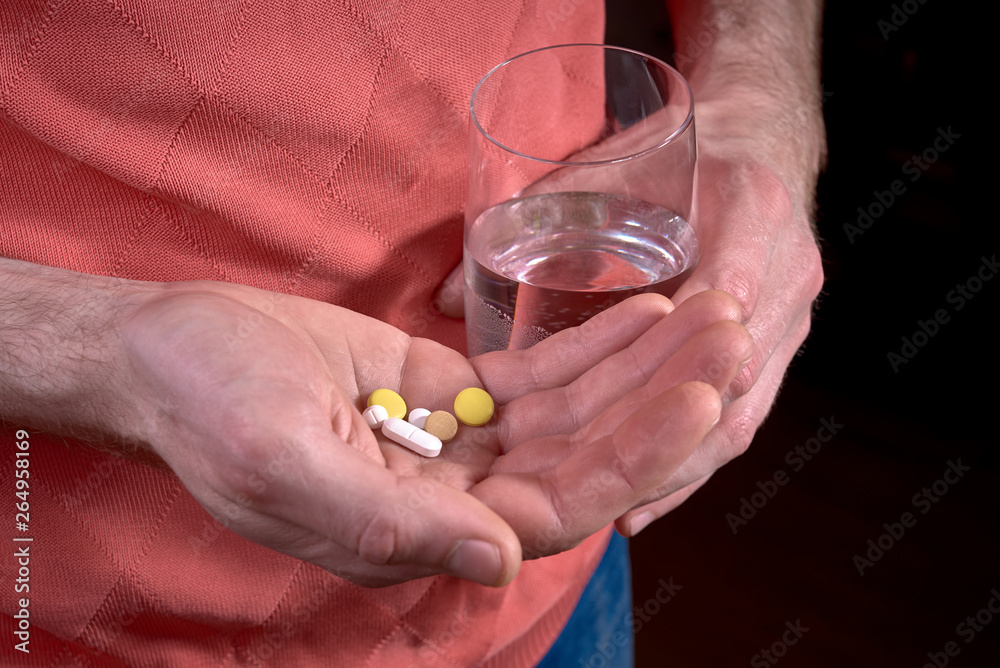 Male holding pills in hand and glass of water Male holding pills in hand and glass of water