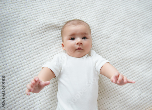 The baby lies on his back and pulls his hands . Top view, look at the camera. Place for text. The child wants to be picked up