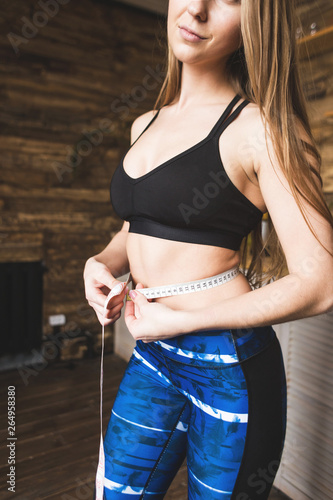 Beautiful young woman in sportswear measures the measured flight waist circumference. Sport, diet and weight loss