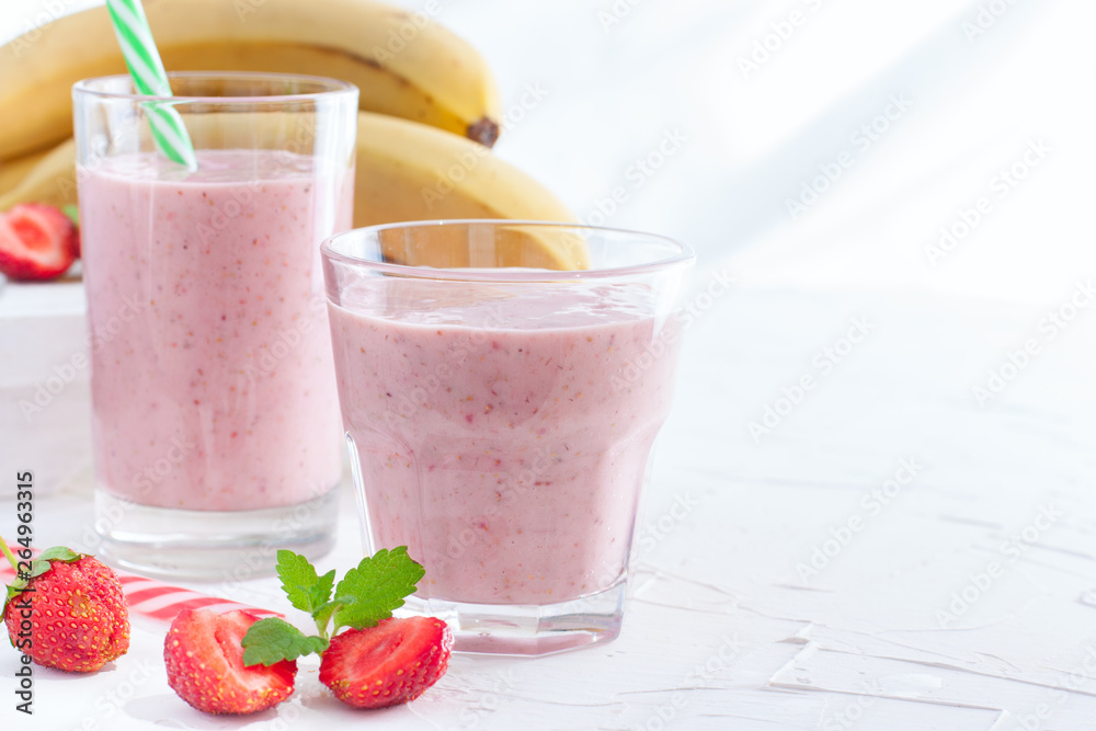Smoothies of fresh strawberries and bananas in glass glasses on a white table, copy space Smoothies of fresh strawberries and bananas in glass glasses on a white table, copy space