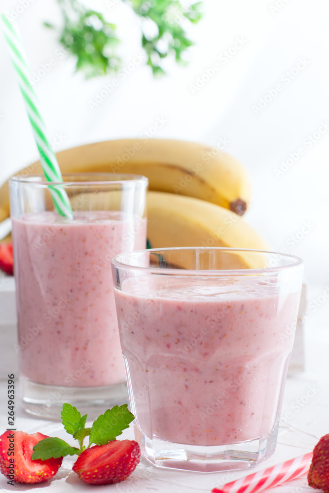 Smoothies of strawberries and bananas in glass glasses on a white table, selective focus Smoothies of strawberries and bananas in glass glasses on a white table, selective focus
