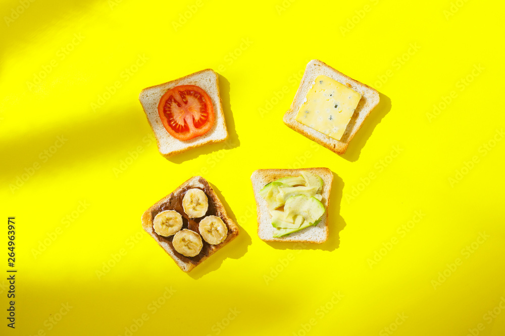 Sandwiches with banana, tomato, avocado, blue cheese on a yellow background. Concept of a healthy breakfast, vitamins, proper nutrition. Natural light, shade from plants. Flat lay, Top view. Sandwiches with banana, tomato, avocado, blue cheese on a yellow background. Concept of a healthy breakfast, vitamins, proper nutrition. Natural light, shade from plants. Flat lay, Top view.
