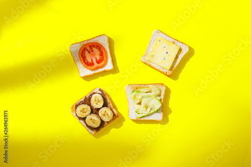 Sandwiches with banana, tomato, avocado, blue cheese on a yellow background. Concept of a healthy breakfast, vitamins, proper nutrition. Natural light, shade from plants. Flat lay, Top view.