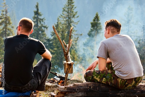 Two men are sitting by the campfire , adventure, travel, tourism and people concept - group of smiling friends sitting on chairs around bonfire in camping