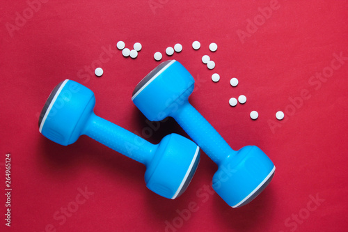 Sport concept. Dumbbells, pills on red background. Minimalism. Top view