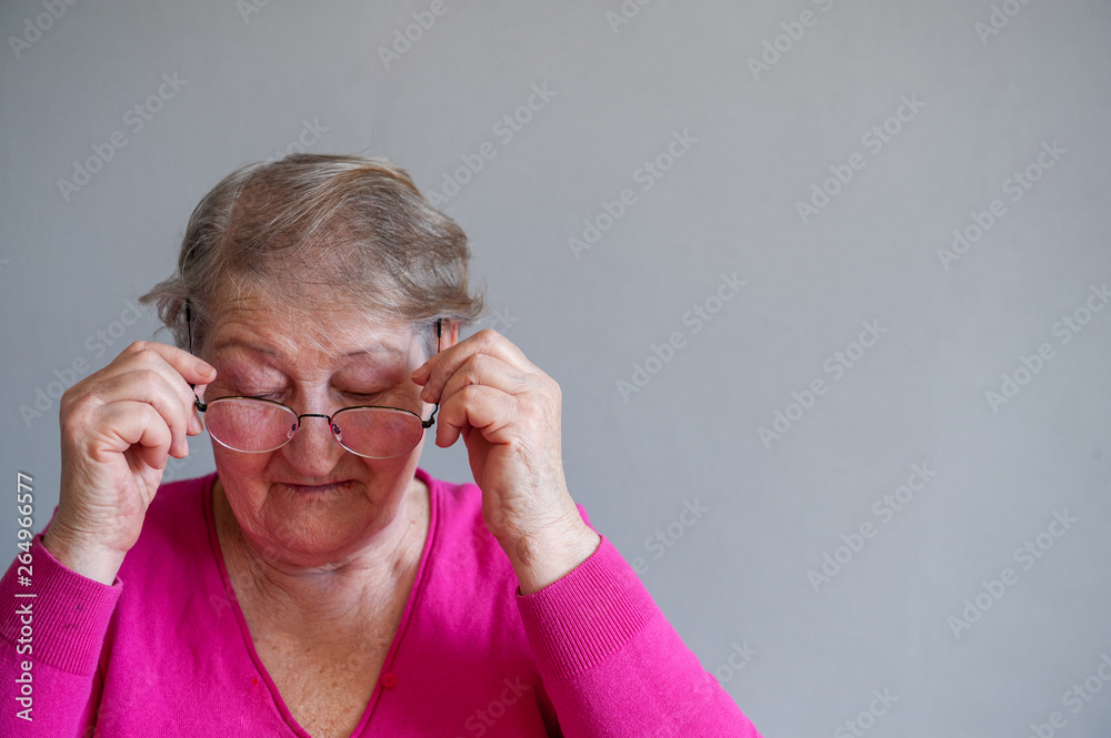 seriously ill elderly woman in pink blouse is sitting on chair and posing for camera trying on new glasses seriously ill elderly woman in pink blouse is sitting on chair and posing for camera trying on new glasses