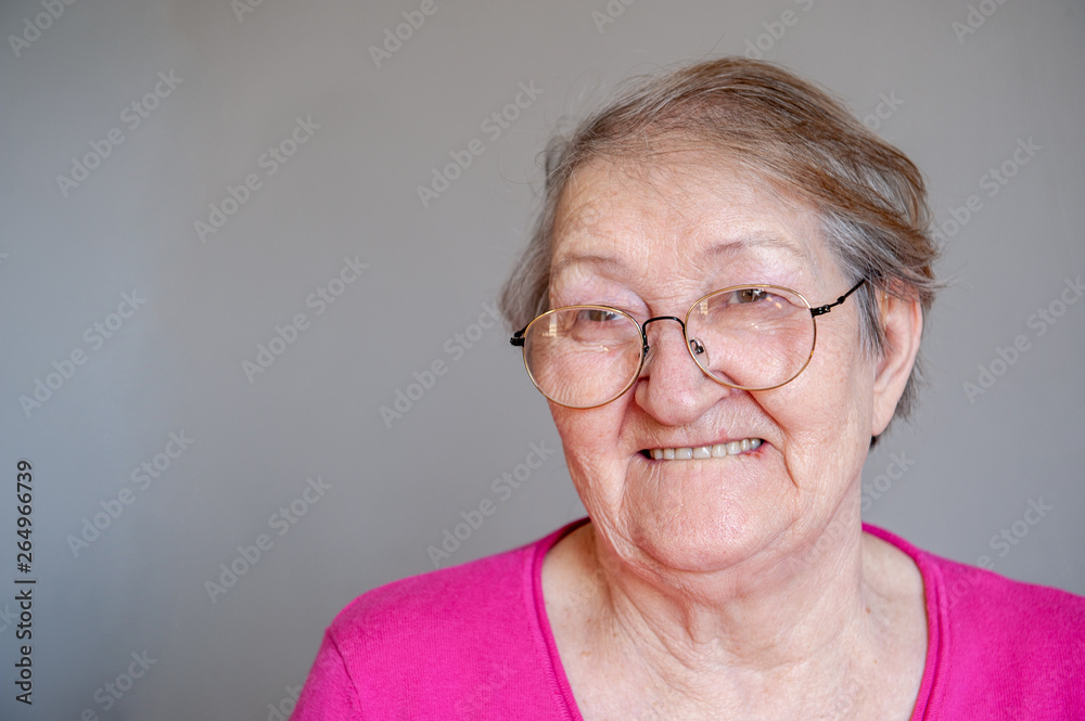 seriously ill elderly woman in pink blouse is sitting on chair and posing for camera trying on new glasses seriously ill elderly woman in pink blouse is sitting on chair and posing for camera trying on new glasses