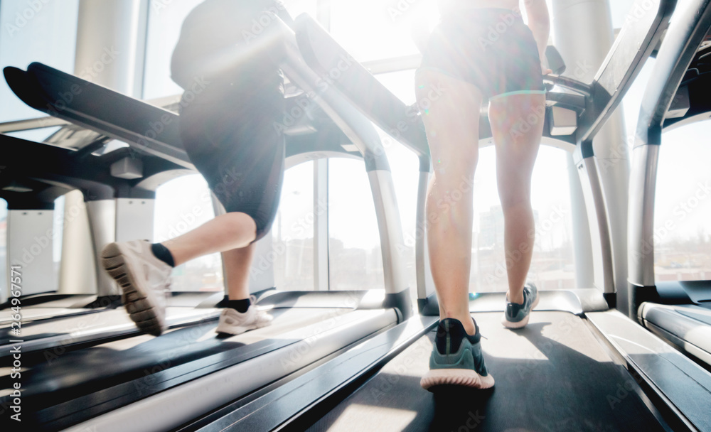 Woman's in sportswear and sneakers running on a treadmill in the gym against the window Woman's in sportswear and sneakers running on a treadmill in the gym against the window