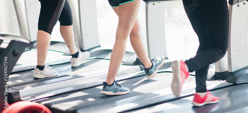 Cropped photo of female legs in sportswear and sneakers running on a treadmill in the gym against the window