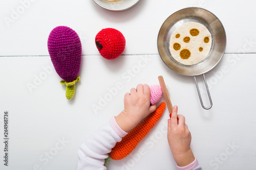 baby hands playing with craft knitted plush vegetables in children kitchen, directly above