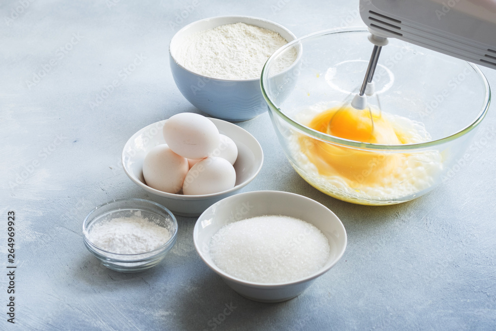 Mixer whipping eggs in a glass bowl and ingredients to create a cake Mixer whipping eggs in a glass bowl and ingredients to create a cake