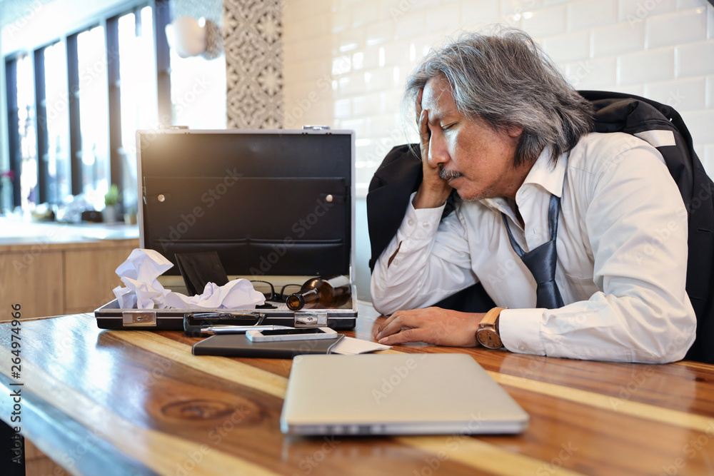 failure businessman wearing black suit sleeping on wood table with alcohol bottle, computer and cell phone on wood table (bankruptcy or unemployed concept) failure businessman wearing black suit sleeping on wood table with alcohol bottle, computer and cell phone on wood table (bankruptcy or unemployed concept)