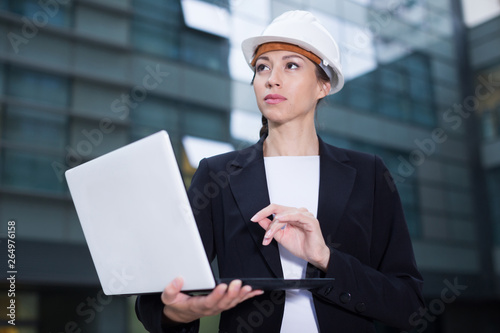 Smiling woman architector in suit and hat is exploring project in her laptop photo