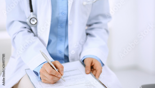 Female doctor writing up medication history records form on clipboard, while sitting at the chair. Physician at work in hospital or clinic. Healthcare, insurance and medicine concept