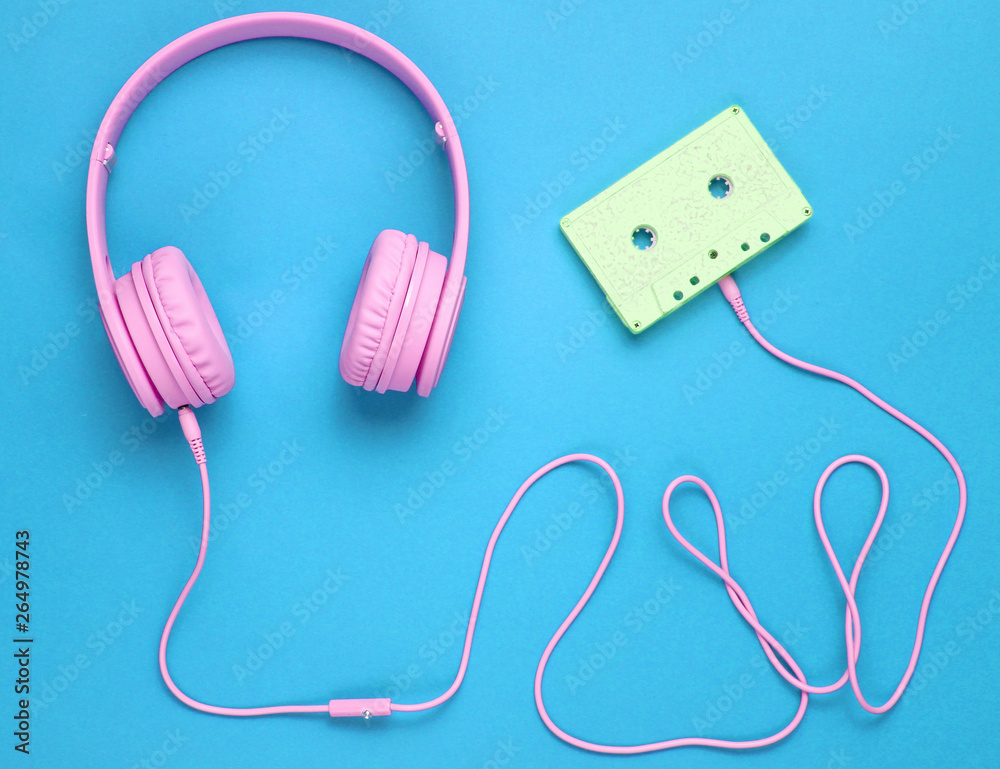 Pink headphones with cable in audio cassette on blue background. Minimalism. Top view Pink headphones with cable in audio cassette on blue background. Minimalism. Top view