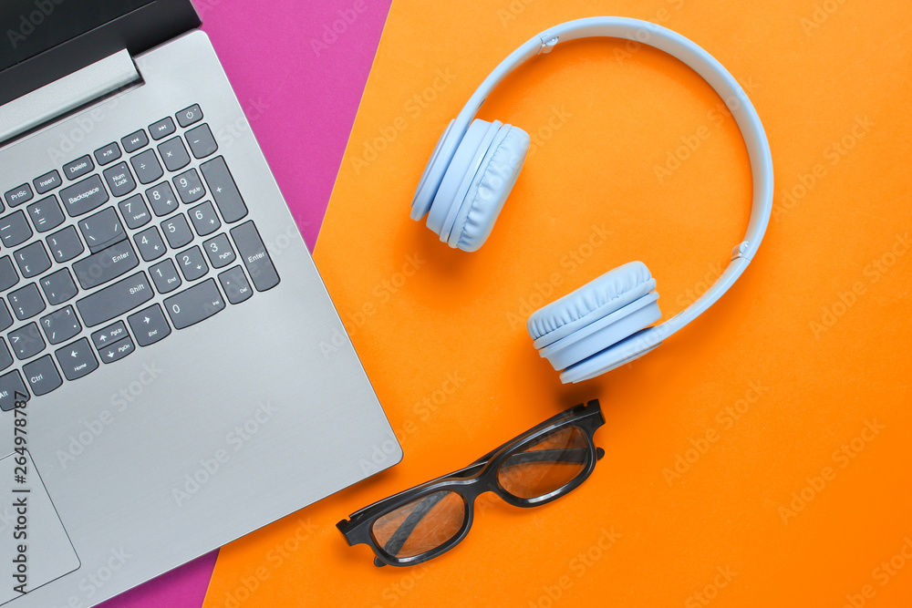 Modern gadgets. Laptop, wireless headphones, 3D glasses on a purple-yellow background.