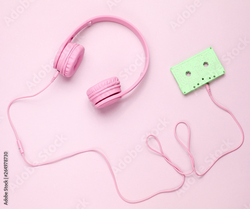 Pink headphones with cable in audio cassette on pink background. Top view