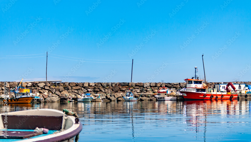 Colorful fishing boats in a harbour on a clear sunny day with blue skies reflected in the calm water.	