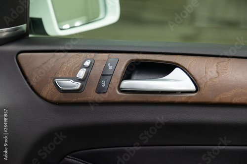 A close-up view of a part of the interior of a modern luxury car with a view of a silver-colored door handle on a chrome finish with brown wood trim after dry cleaning. Auto service industry.