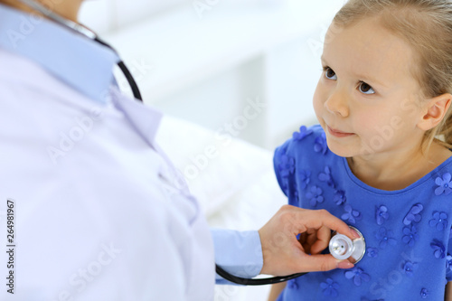 Doctor examining a little girl by stethoscope. Happy smiling child patient at usual medical inspection. Medicine and healthcare concepts