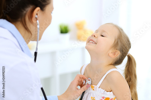 Doctor examining a little girl by stethoscope. Happy smiling child patient at usual medical inspection. Medicine and healthcare concepts