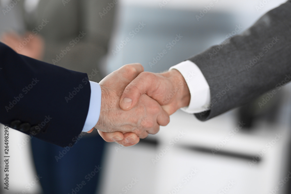 Business people shaking hands at meeting or negotiation, close-up. Group of unknown businessmen and women in modern office at background. Teamwork, partnership and handshake concept