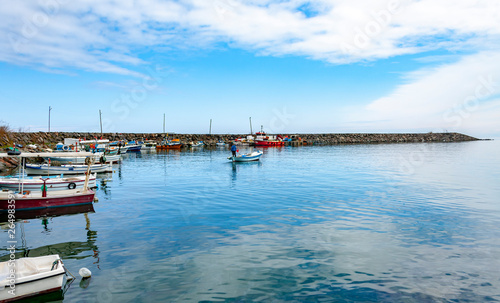 Colorful fishing boats in a harbour on a clear sunny day with blue skies reflected in the calm water. © 0804Creative