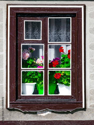 A wooden window outside the house with flowering geranium flowers in an old traditional European house. photo