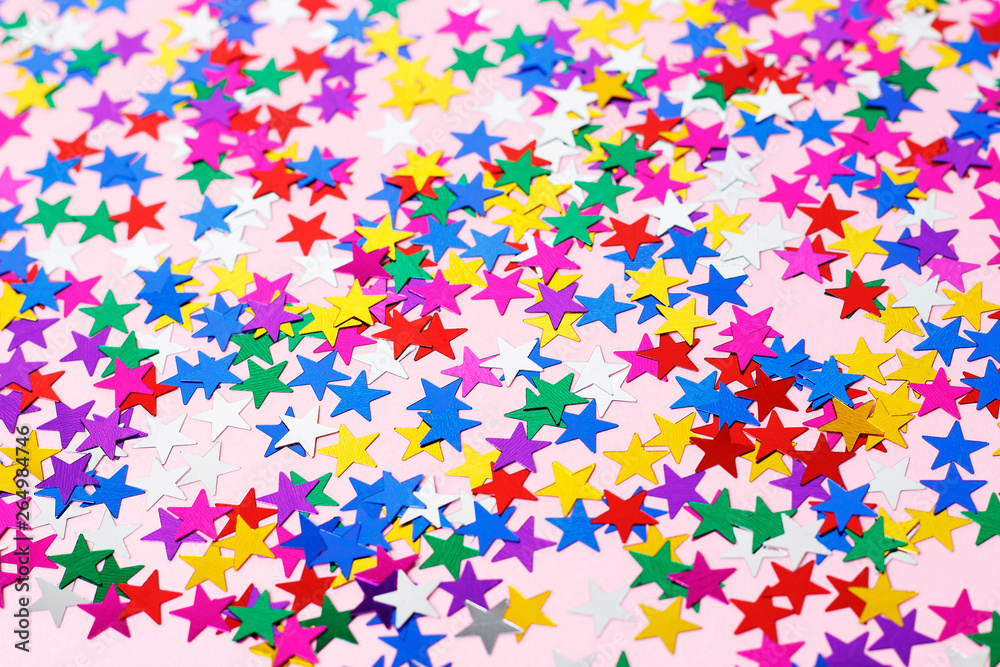 Multicolored stars of confetti on a pink background, copy space
