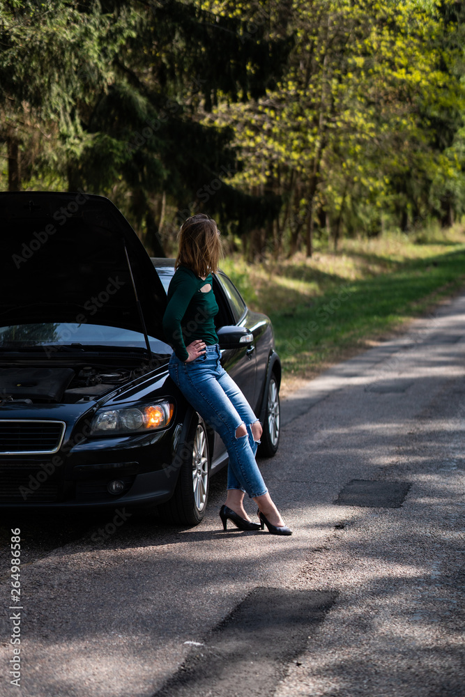 Young woman standing next to a broken car on countryside. Woman's car broken. Woman trying to fix a broken car. Despaired woman trying to fix broken car. Young woman standing next to a broken car on countryside. Woman's car broken. Woman trying to fix a broken car. Despaired woman trying to fix broken car.
