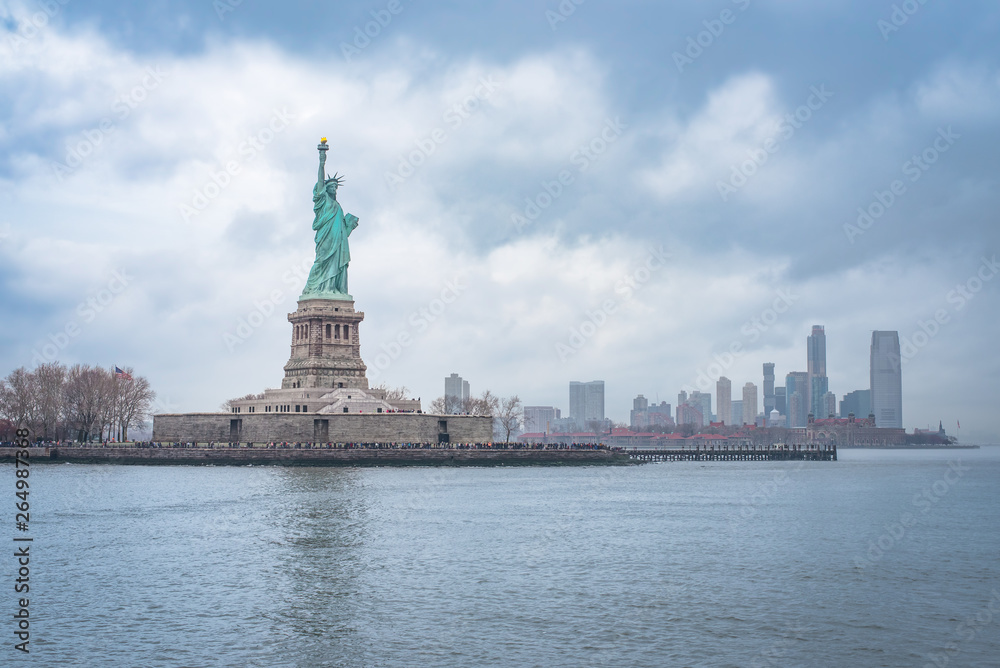 Liberty Island and Statue of Liberty under a dramatic sky with Ellis Island and City Skyline 